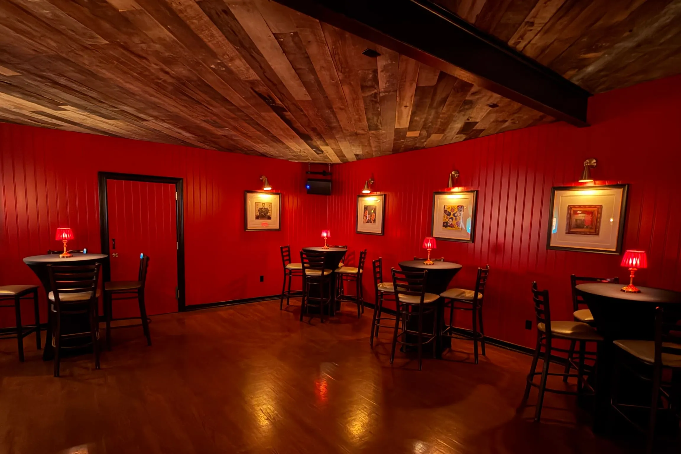The back room at FKA: Formerly Known As set for an event, with red paneled walls, cocktail tables, framed album art, and red lamps