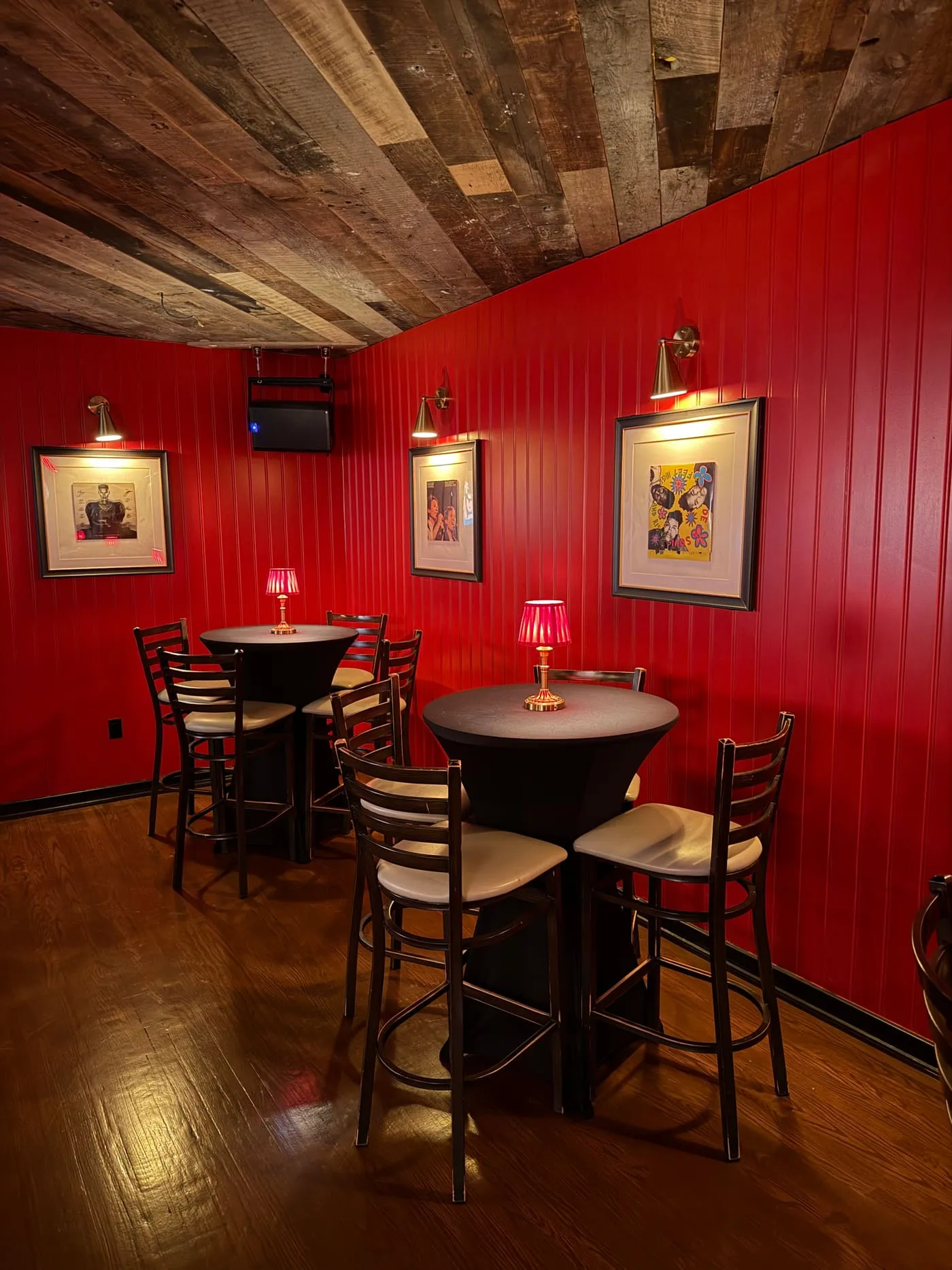 Cocktail tables with red lamps under framed album covers in the back room at FKA: Formerly Known As