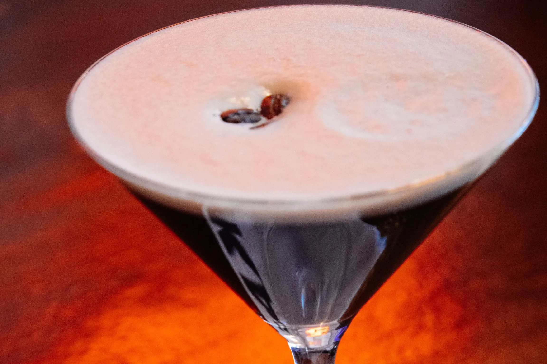 Close-up of an espresso martini with coffee beans on the foam, glowing on the wooden bar at FKA: Formerly Known As